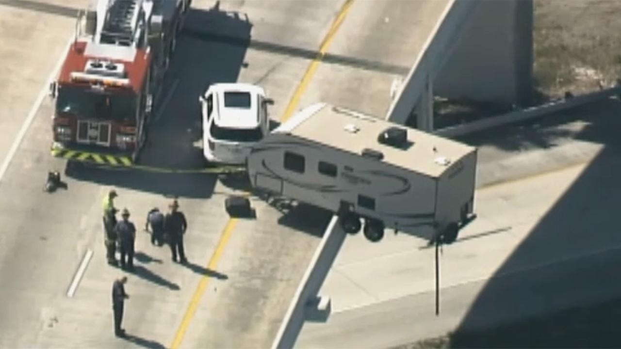 Camper trailer dangles precariously over highway overpass