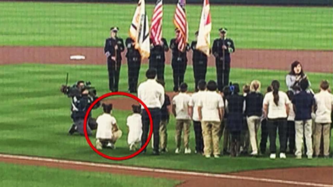 Elementary students kneel while performing national anthem