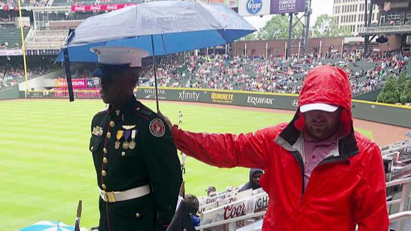 Baseball fan holds an umbrella over a JROTC cadet
