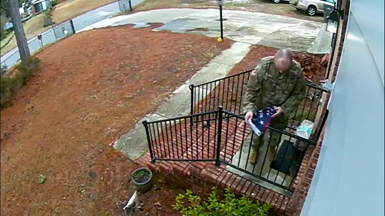 Man in military garb folds flag torn from pole during a storm, returns it to owners porch